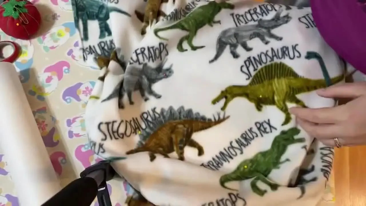 Hands smooth a dinosaur-print fleece tie blanket over a hooped stabilizer, demonstrating the floating method before stitching.