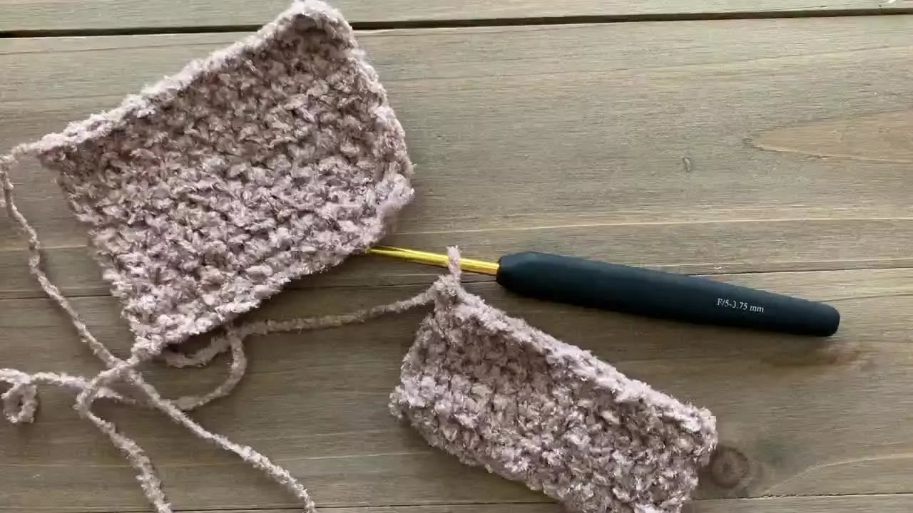 Crochet hook, stitch markers, and chenille yarn swatches laid on a wooden table.