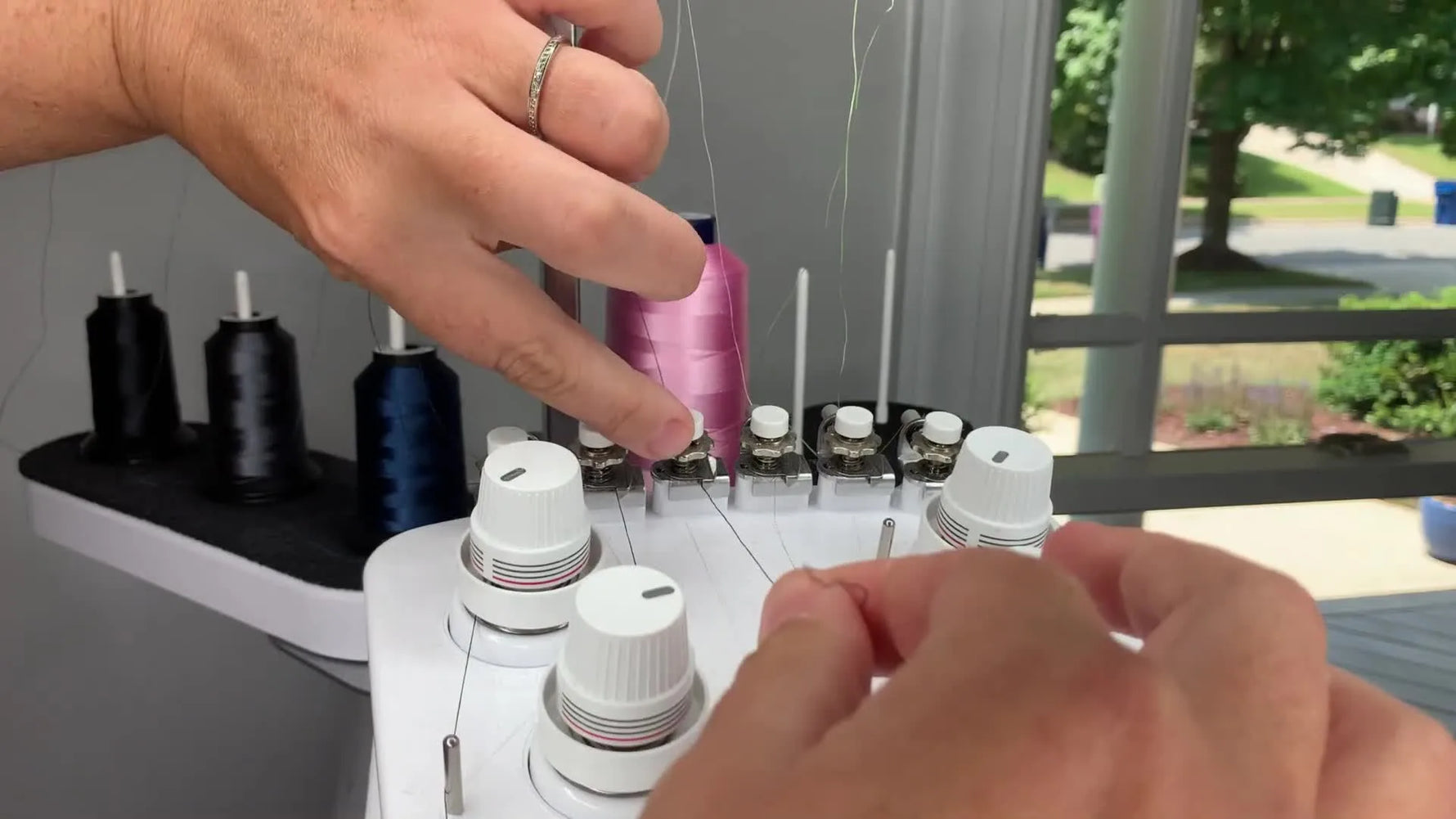 An extreme close-up shows embroidery thread being “flossed” firmly into the Baby Lock Intrepid’s white tension knob assembly—the make-or-break moment for clean stitching.