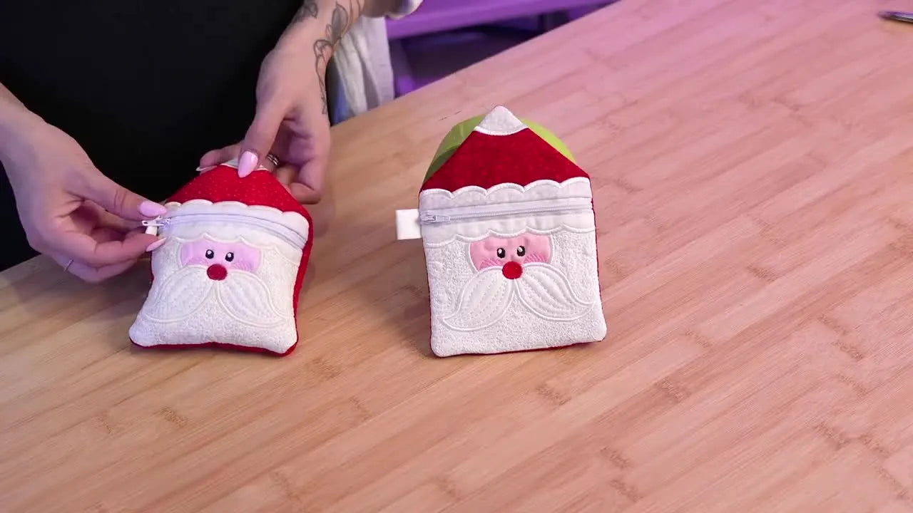 The host holds up two finished Santa-themed in-the-hoop zipper bags, showing crisp satin borders and a cleanly functioning zipper.
