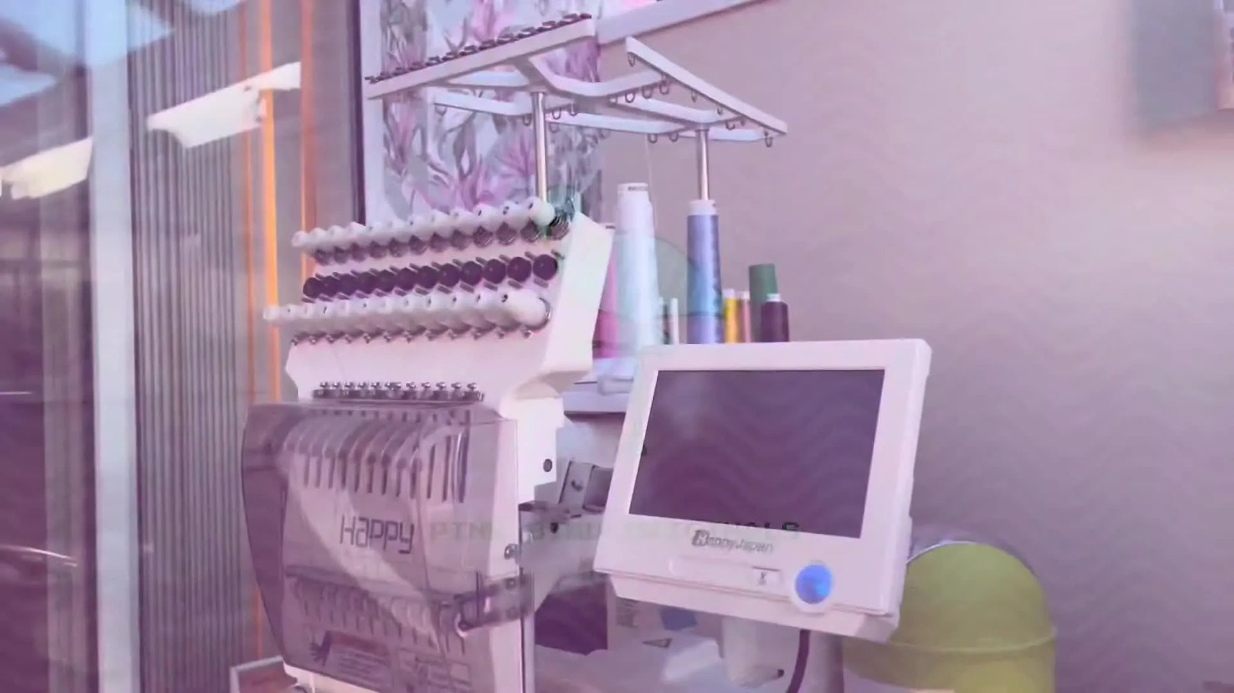 A side profile view of a white Happy Japan multi-needle embroidery machine on a studio desk, ready for production work.