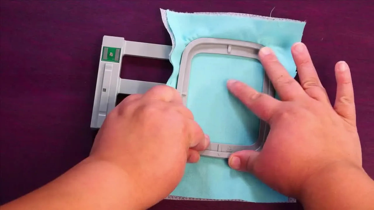 Hands pressing the inner embroidery hoop into the outer hoop, stretching the fabric taut.