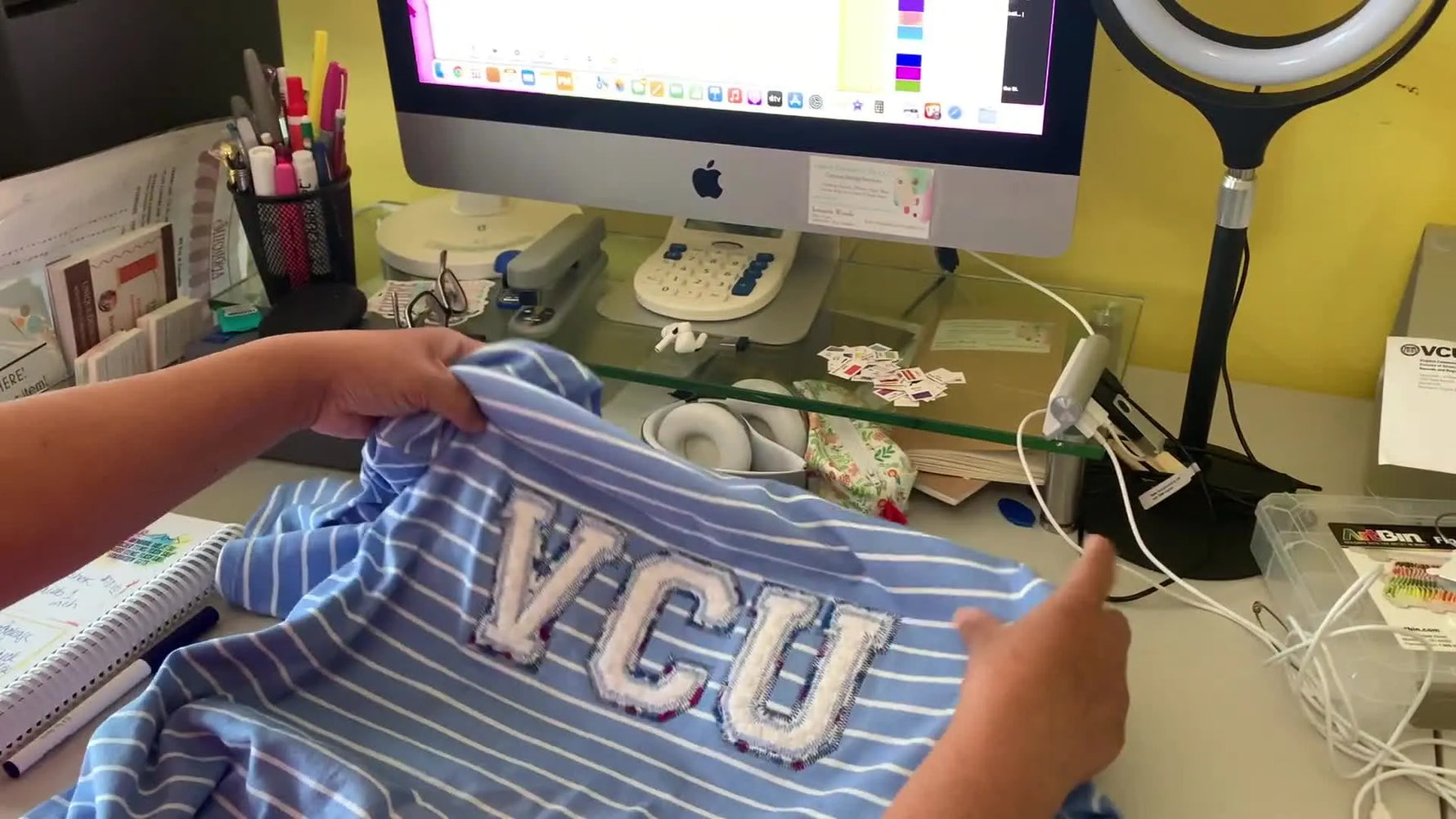 A close-up of a blue striped shirt featuring “VCU” towel-scrap appliqué letters, showing the finished zigzag/satin-style edge stitching.
