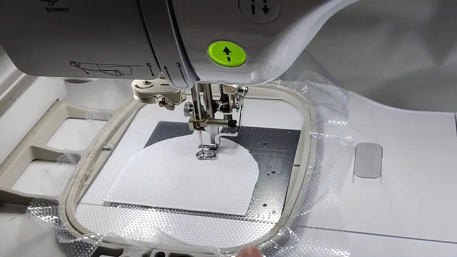 Close-up of the Brother Luminaire stitching the black sewing machine logo inside the badge shape during the main embroidery run.