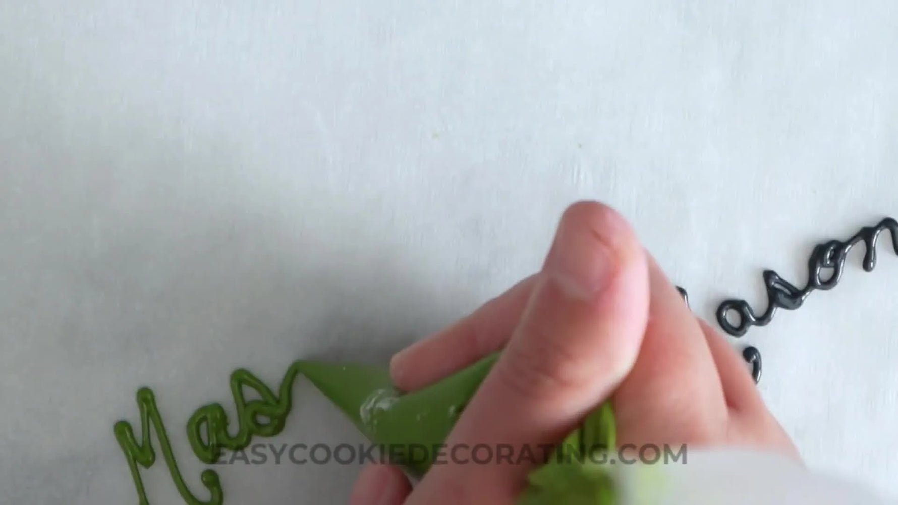 A close-up shot of hands practicing royal icing cursive on parchment paper, ensuring proper flow and consistency before decorating.