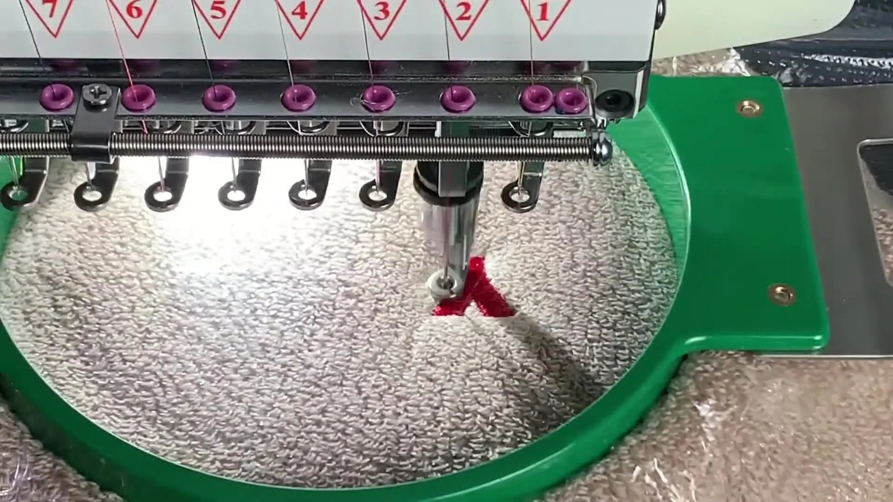 A close-up of the YunFu machine stitching a red satin letter onto a thick towel through clear water-soluble topping.
