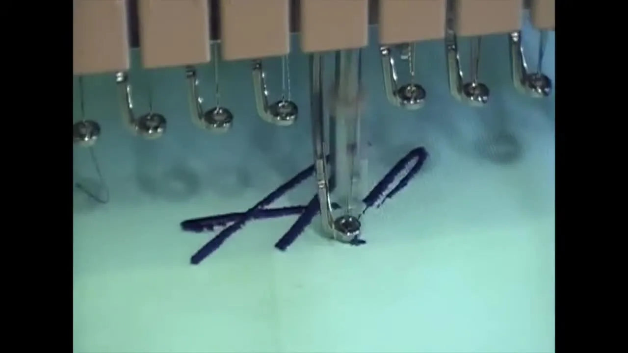 Close-up action shot of a multi-needle embroidery machine stitching a name onto mint green fabric.