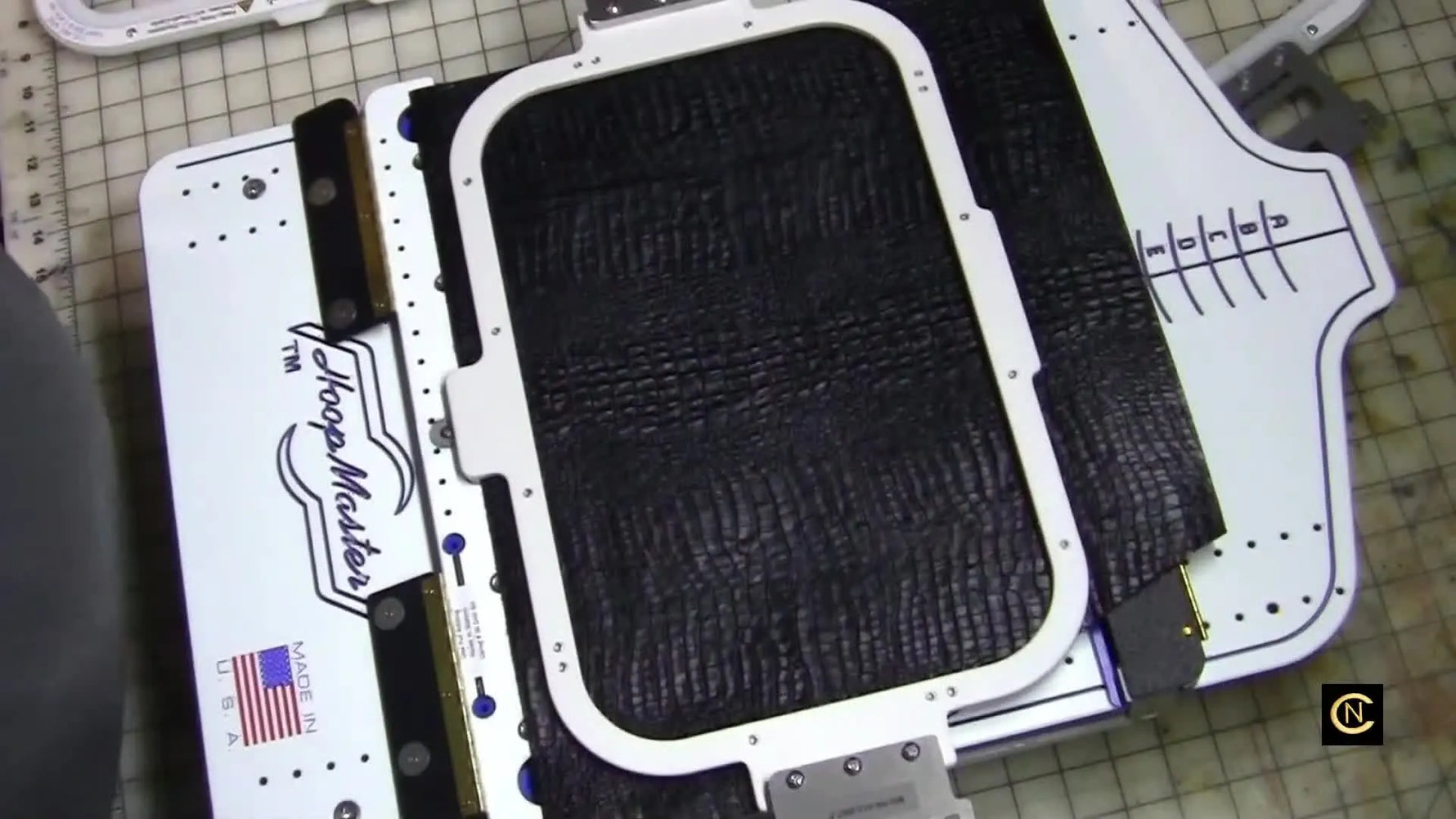 Overhead view of a magnetic hoop snapping shut on a tote bag inside a hooping station fixture for fast, repeatable alignment.
