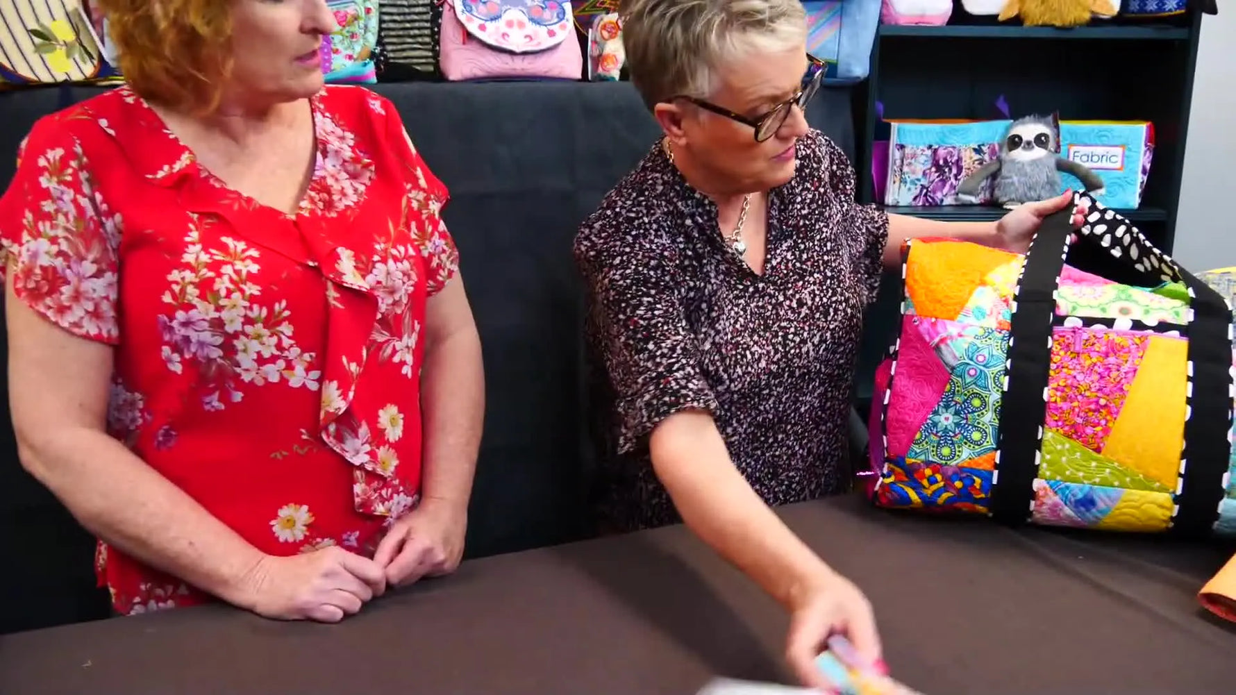 A host holds up a colorful patchwork-style embroidered duffel bag made from multiple in-the-hoop panels.