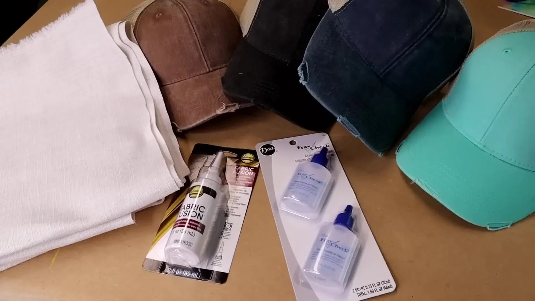 Overhead shot of various hat-making materials including hats, fabric, and glue bottles.