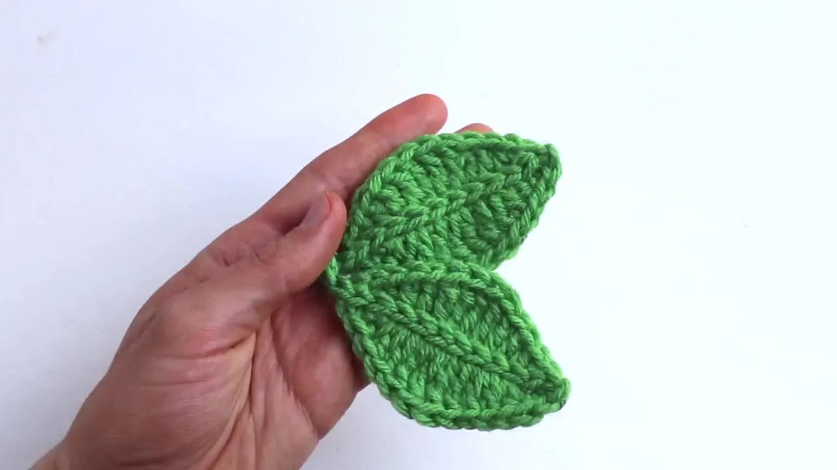 Hands holding two crocheted green cherry leaves