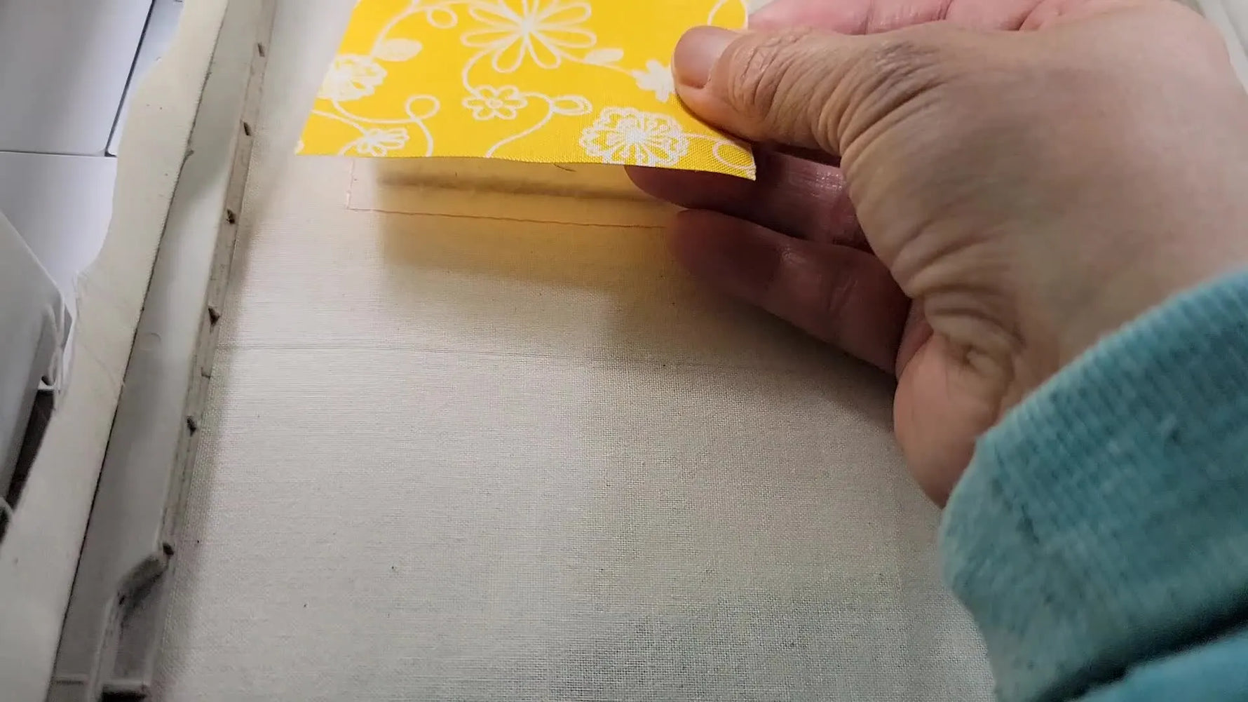 A close-up of the Brother embroidery machine stitching a tack-down line on a yellow fabric filler block inside the hoop.
