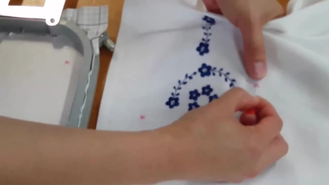 A close-up shows a pin placed through a stitched registration cross to precisely align the second hooping over the first.