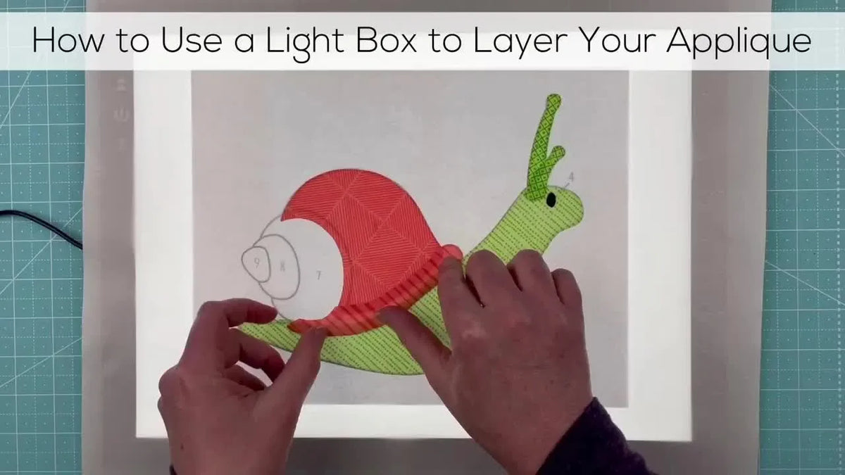 Hands assembling applique pieces on a light box