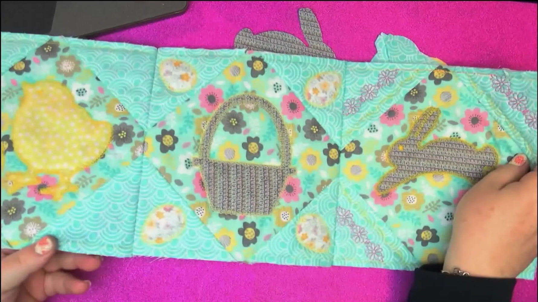 A finished Easter-themed table runner shows four appliqué blocks with baskets, bunnies, eggs, and chicks stitched cleanly and evenly.