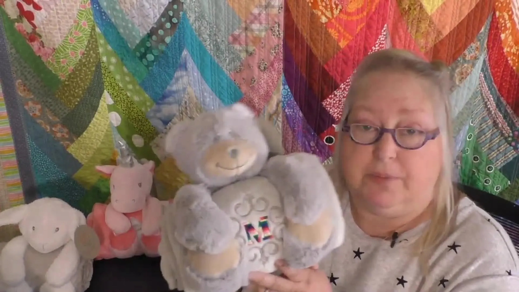Michelle holds the grey bear hugger while showing a clean, centered monogram stitched on the plush blanket.