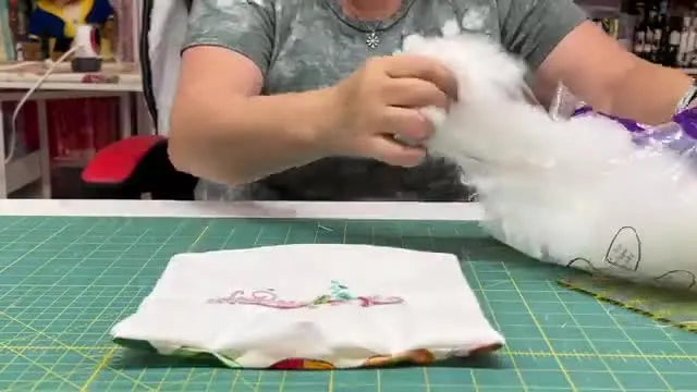 The host holds up two finished glitter vinyl appliqué pillows, showing the sparkle and clean edges after the tack-tear-press method.