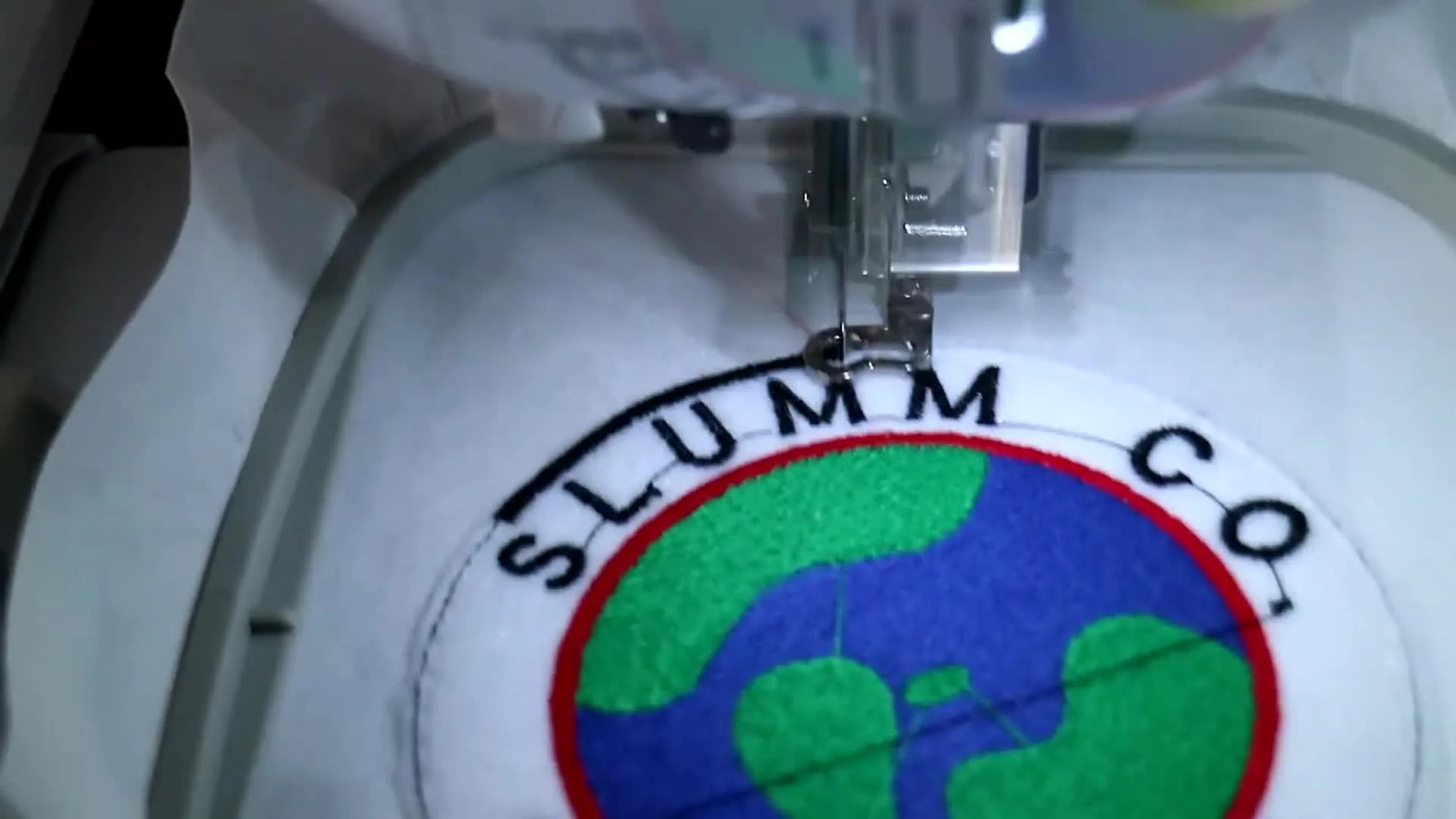 The finished circular patch is held up while still hooped, showing crisp borders, dense fills, and clean lettering.