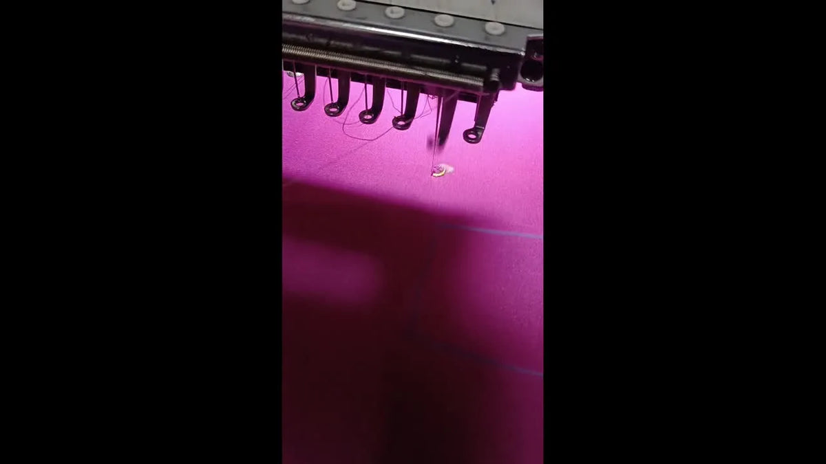 Embroidery machine stitching a gold satin border around a freshly punched hole in pink fabric.