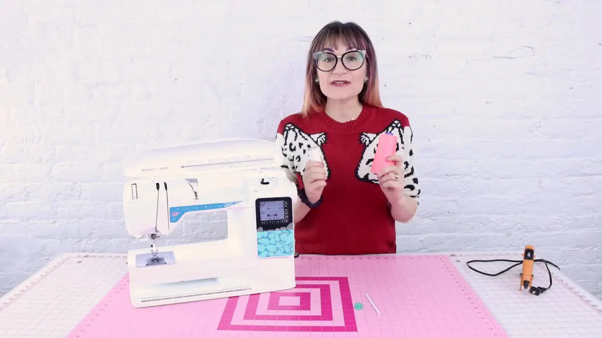 Woman holding large and small thread spools beside sewing machine