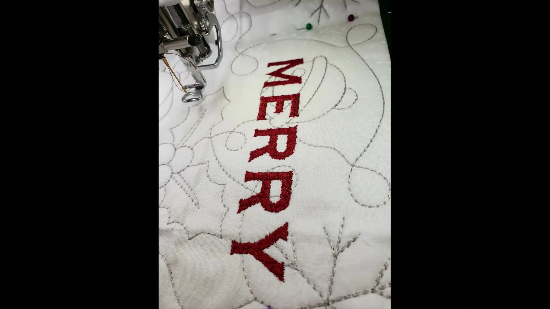 A close-up of the word “MERRY” stitched cleanly in red on a white quilted background, showing accurate placement and crisp coverage.