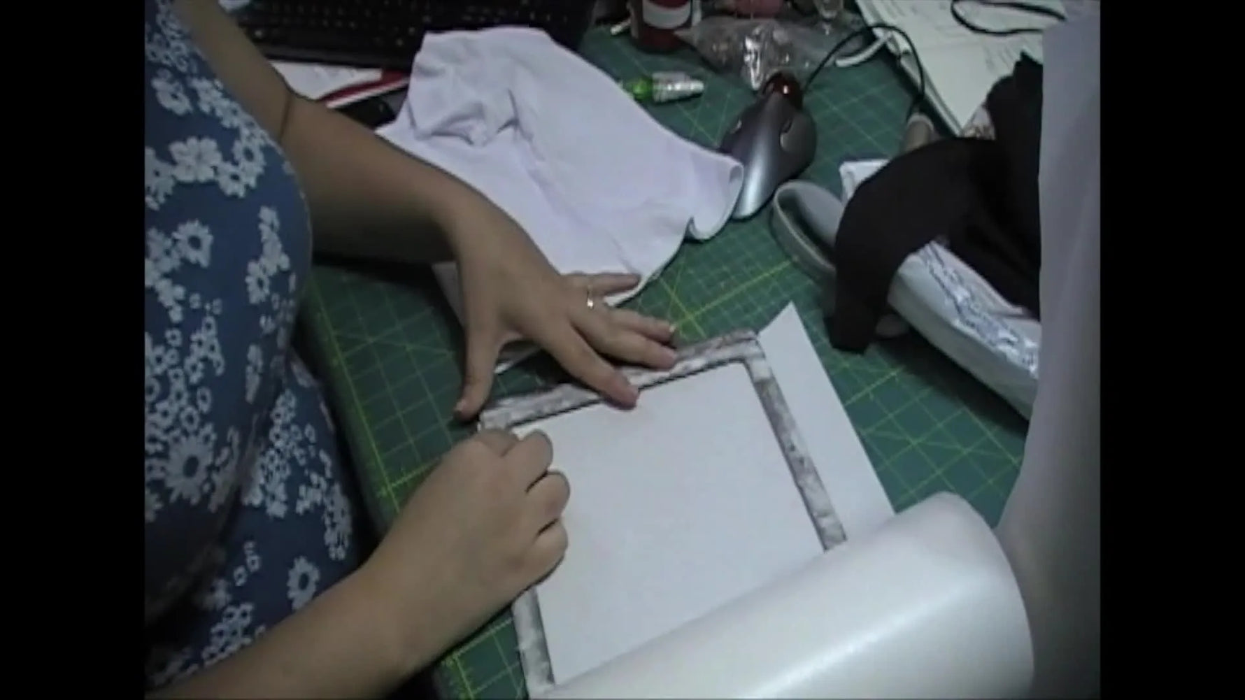 Hands align a metal Fast Frame over a fresh sheet of sticky-back stabilizer on a cutting mat, showing the exact moment adhesion is set up for success.
