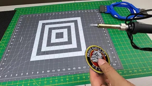 A close-up of a soldering iron sealing the cut edge of an embroidered patch to prevent fraying and create a smooth, rigid finish.