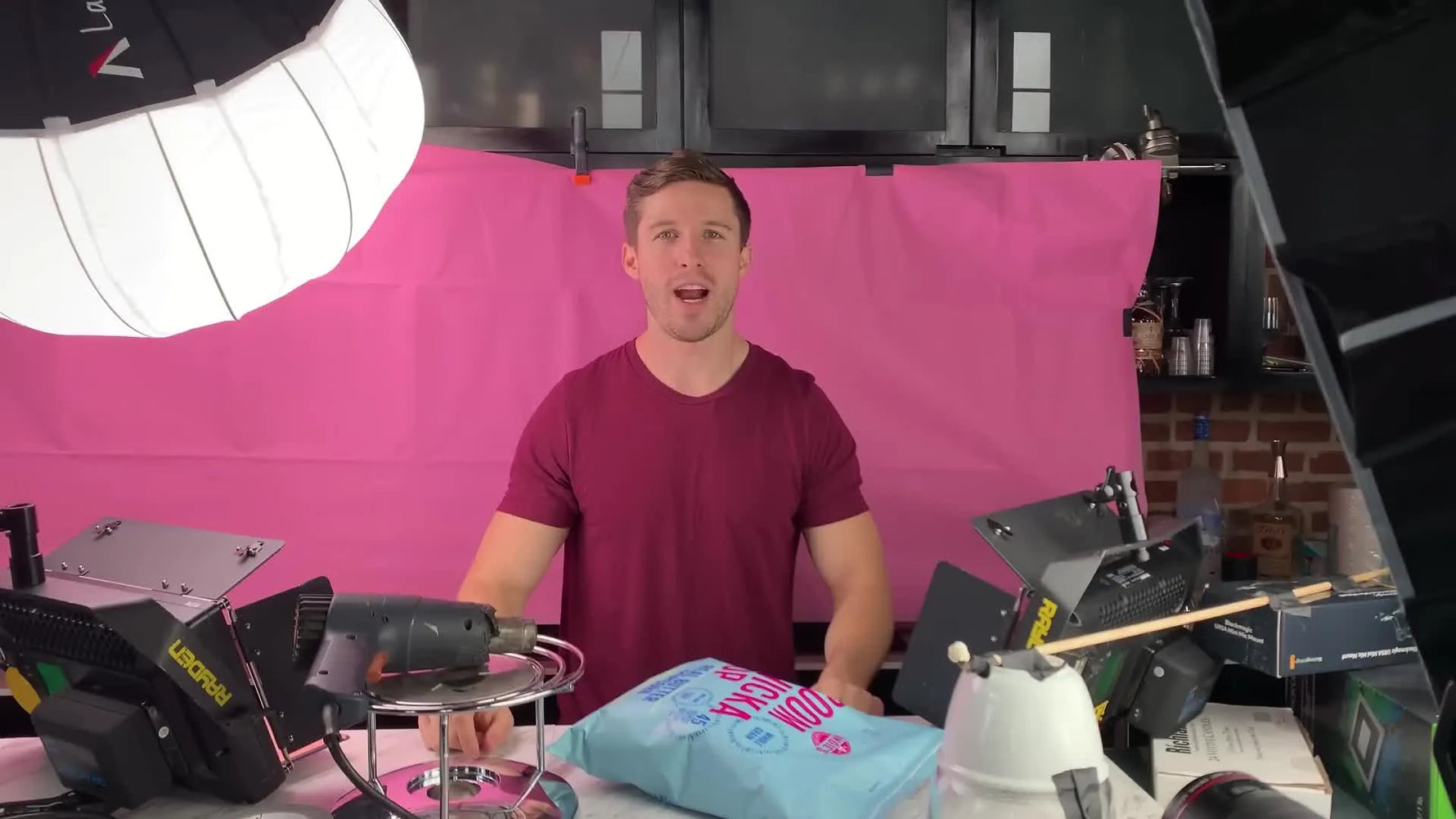 Man holding a bag of Boom Chicka Pop popcorn in a studio setting with lighting equipment.