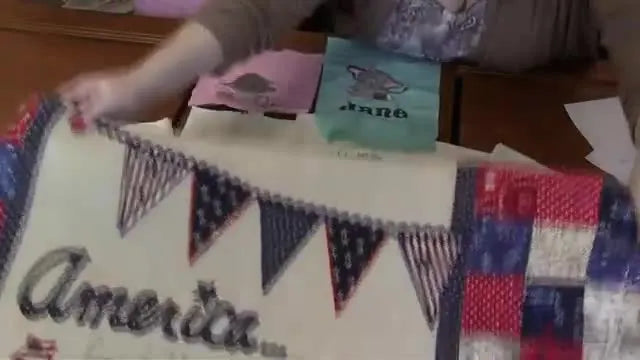 Donnett holds up a patriotic Kimberbell pillow runner featuring rickrack, quilting-in-the-hoop texture, and dimensional pinwheel elements.