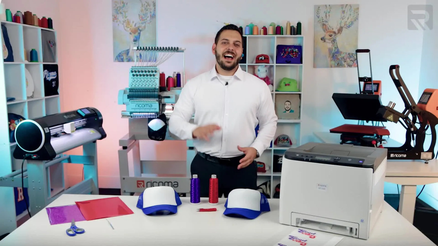 A side-by-side cap decoration setup showing an embroidery machine, a white toner printer, and a vinyl cutter with sample hats ready for production.