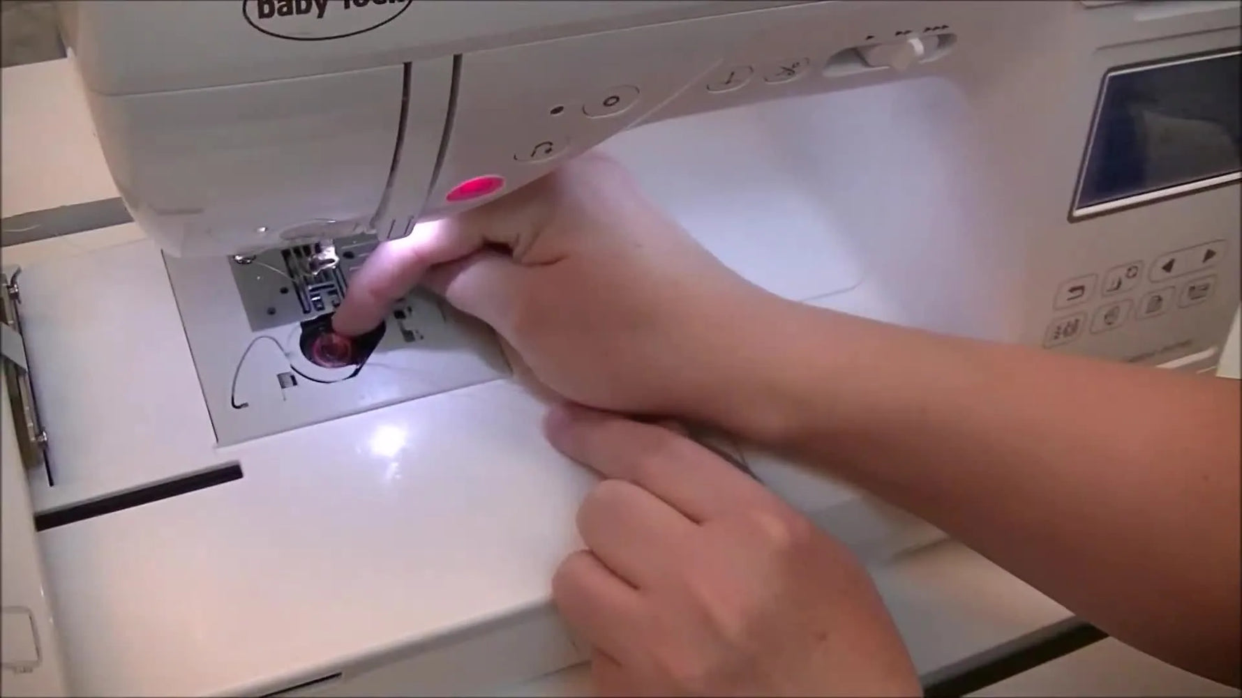 A close-up shows a finger holding a drop-in bobbin firmly in place while the bobbin thread is guided into the correct tension path.