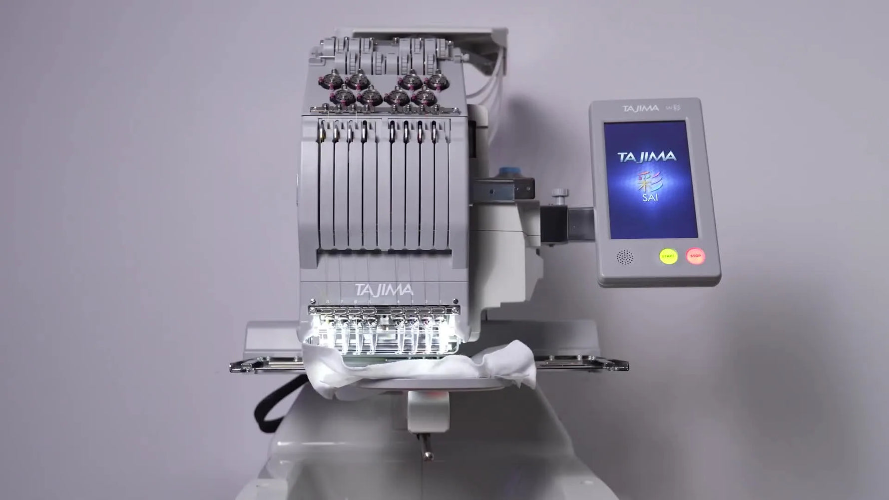 A front view of the Tajima Sai 8-needle compact commercial embroidery machine with the touchscreen lit and the needle area ready to stitch.