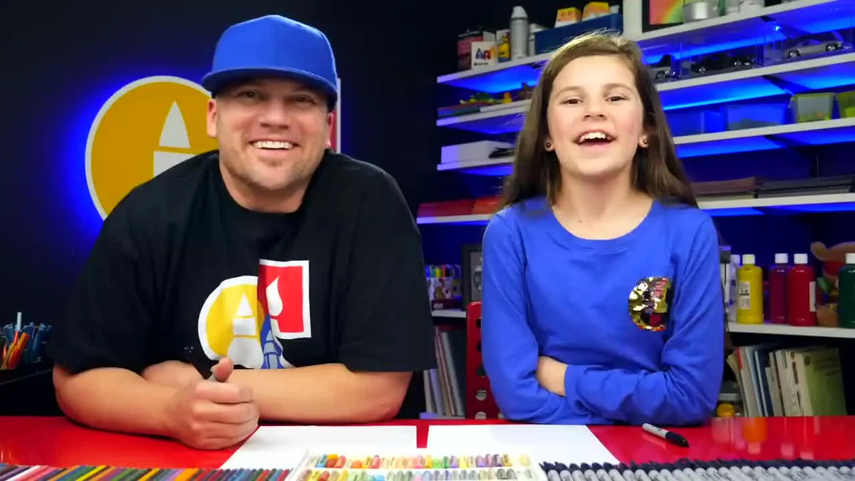 Father and daughter smiling at the camera with art supplies on a red table.