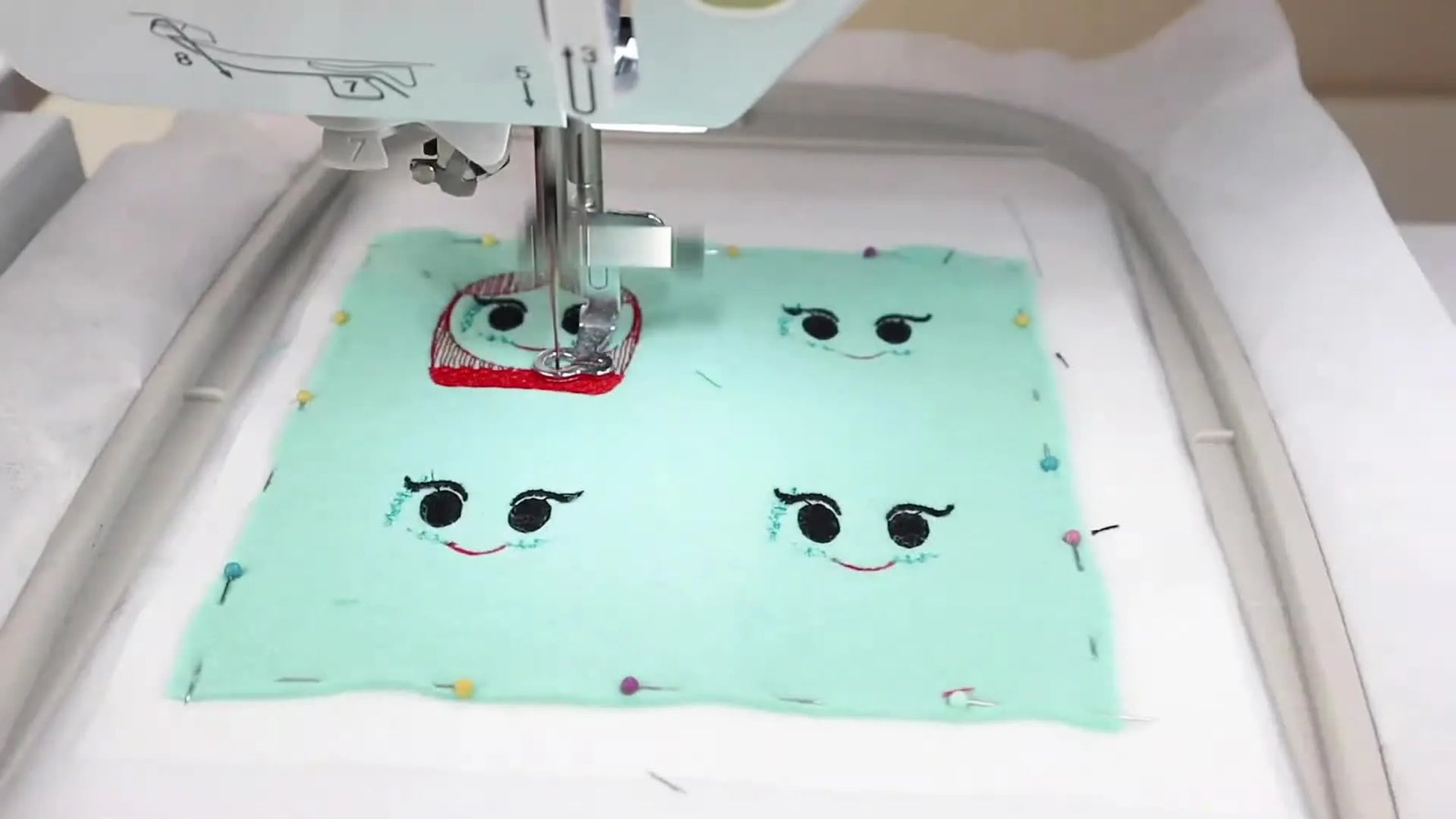 Four completed feltie faces stitched on a single felt sheet inside the hoop, showing the payoff of running a grouped file.