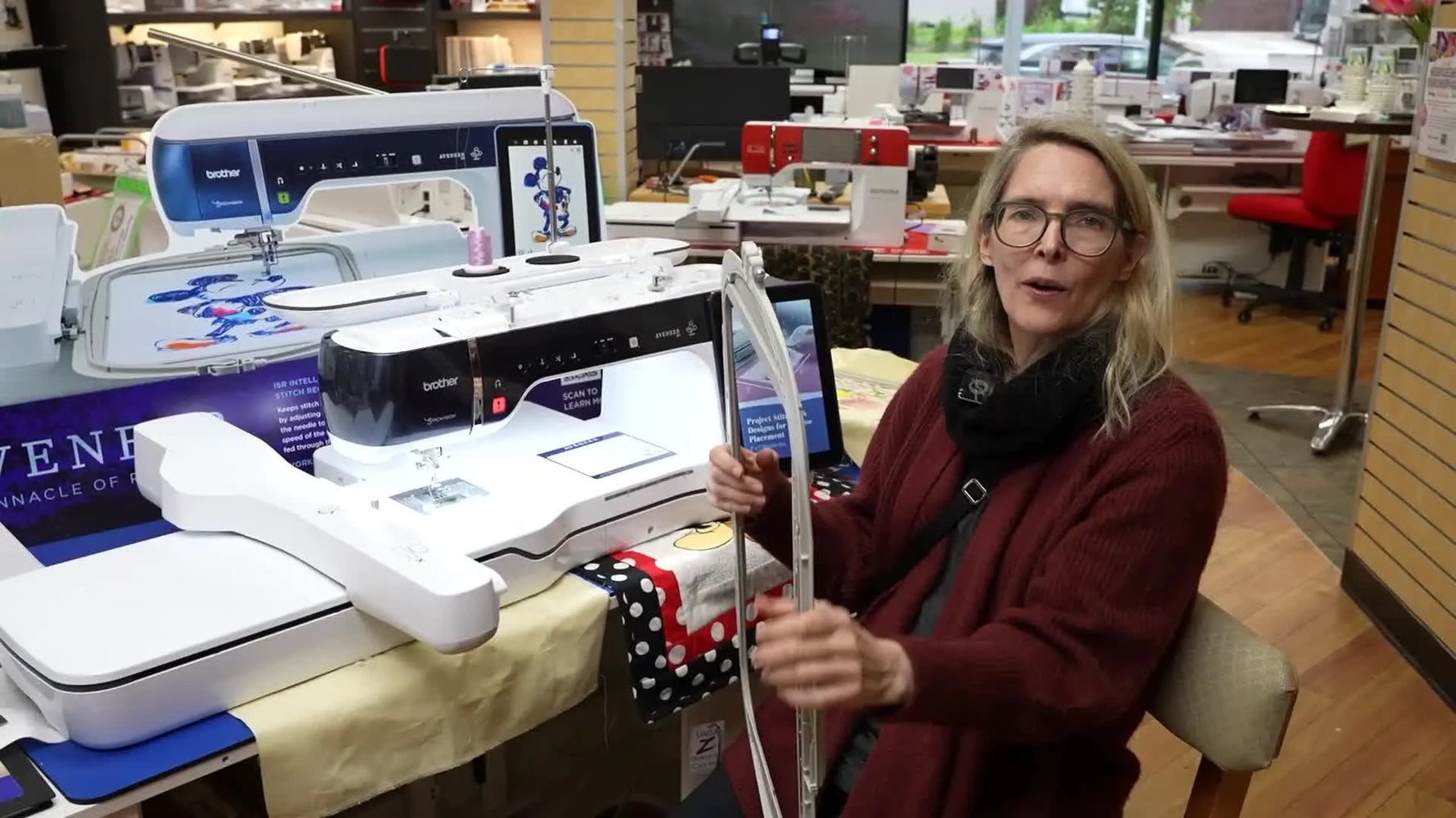 A wide shot of Debbie seated at the Brother Aveneer EV1 with the machine and its large screen visible.