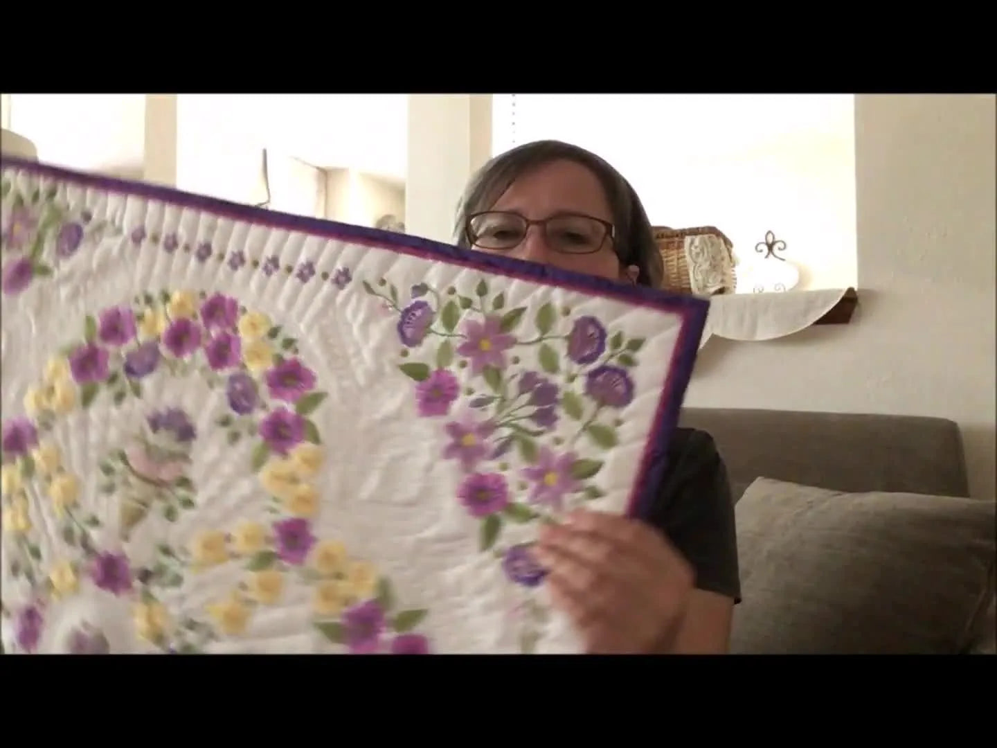 An award-winning floral ring quilt is held up to show how many separate hoopings can be blended into one seamless, professional-looking layout.