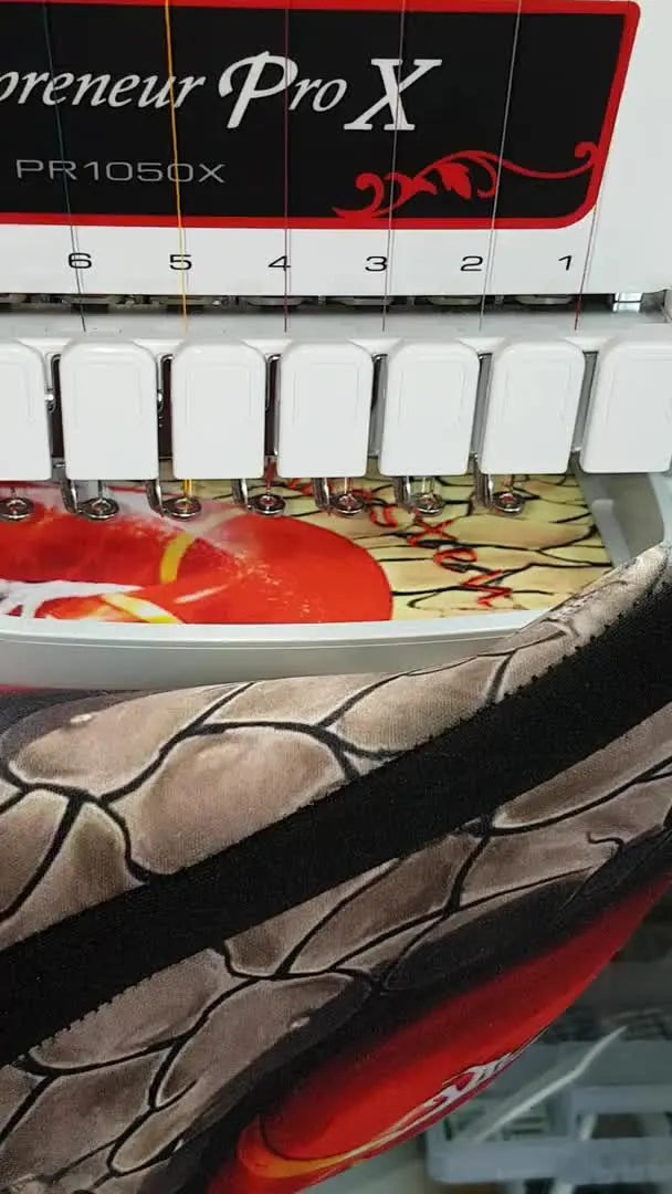 The finished laptop sleeve is shown on a table beside the hoop and scissors, highlighting the completed red text embroidery on a printed background.
