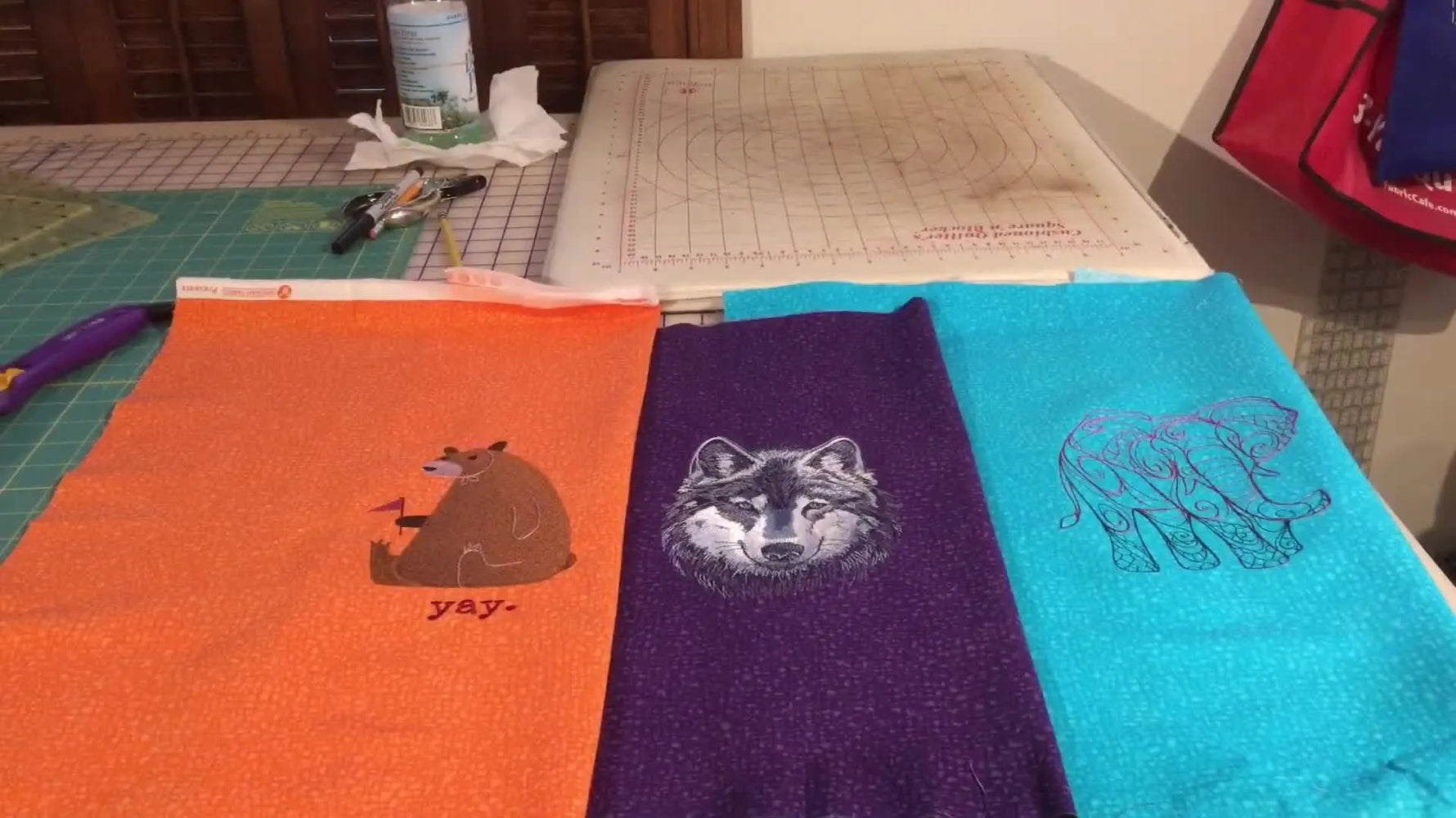 Three finished embroidery hoops on teal, purple, and orange fabric are laid side-by-side for a direct stabilizer-and-stitch-count comparison.