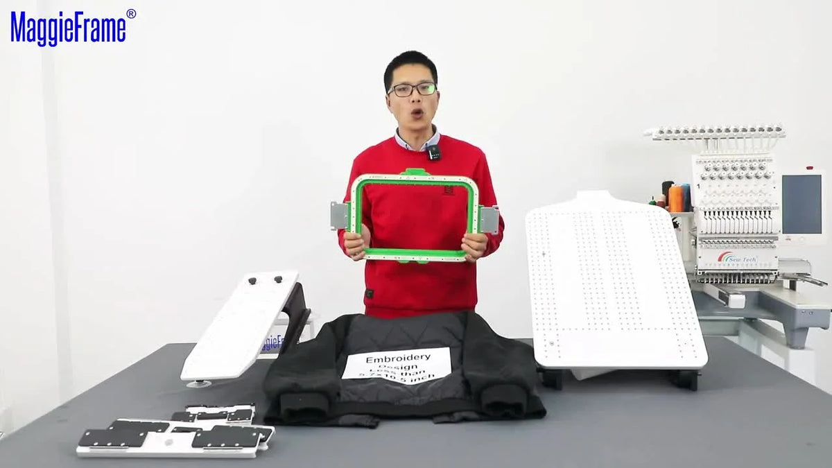 Presenter holding up a green and silver 7.7x12.5 inch MaggieFrame magnetic hoop in front of an embroidery setup.