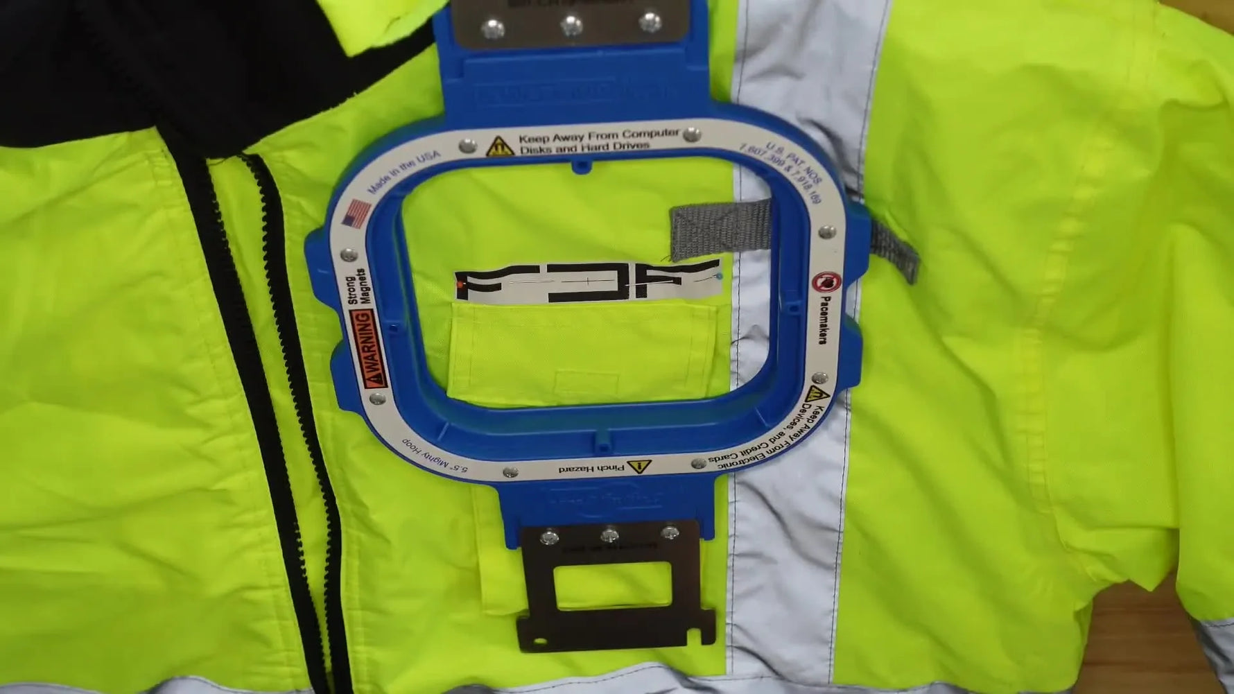 Woman's hands guiding an unzipped yellow work jacket onto the Mighty Hoop Freestyle station for hooping.