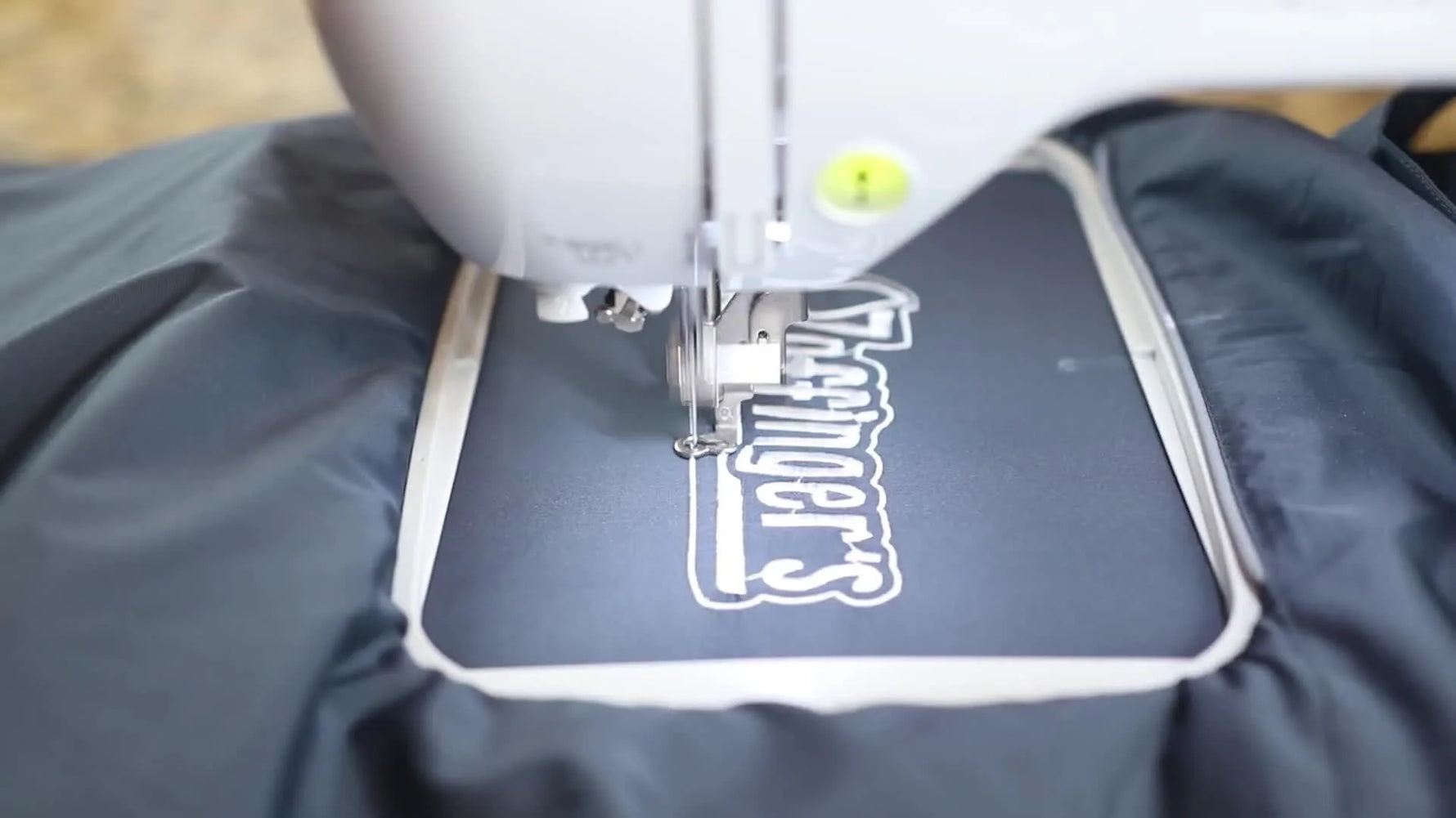 A close-up of the Brother PE800 actively stitching a logo onto a slippery windbreaker inside a 5x7 hoop.