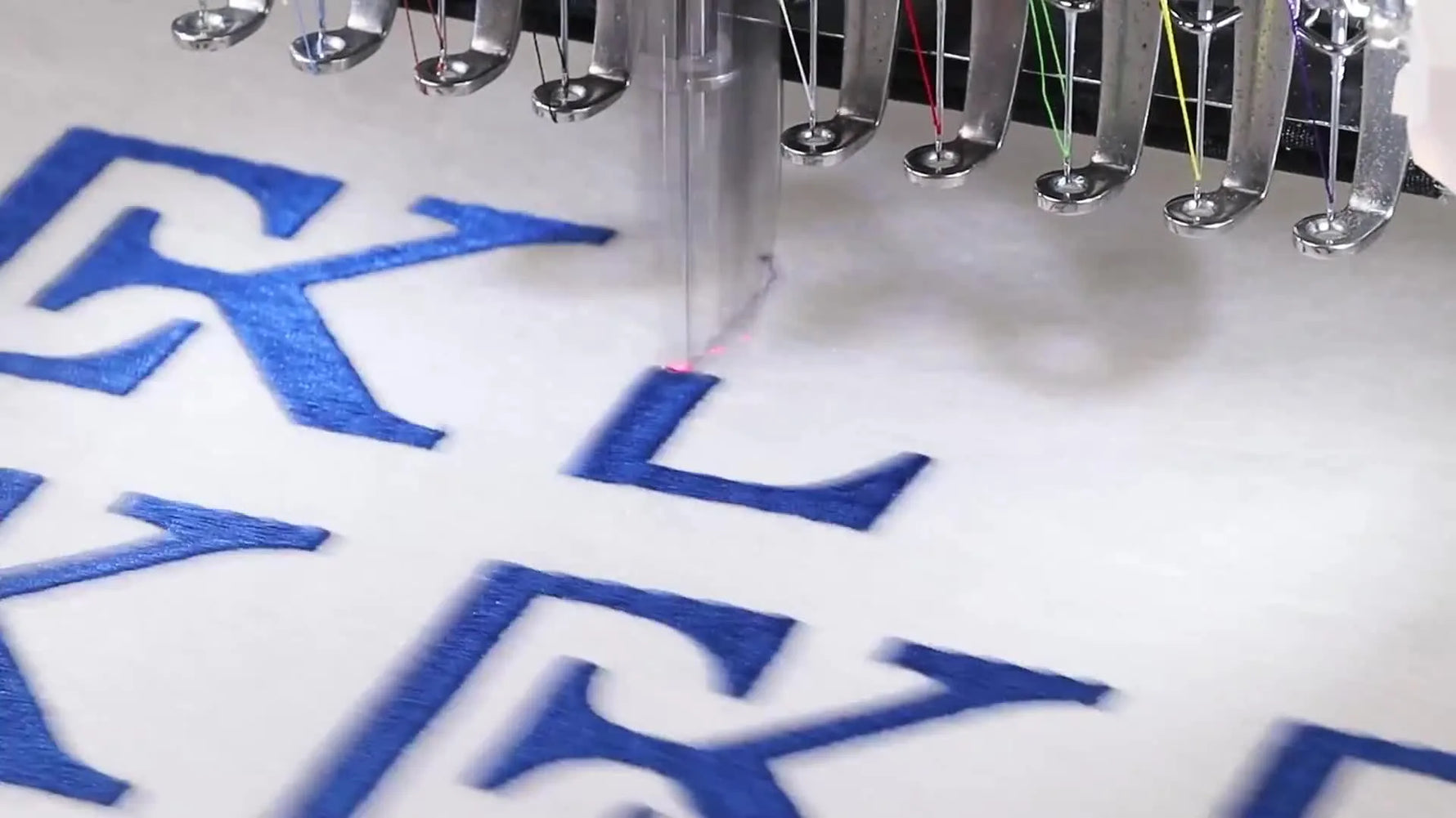 A Smartstitch multi-needle machine shows six finished “K” logos stitched in a 3×2 grid on one hooped fabric piece.
