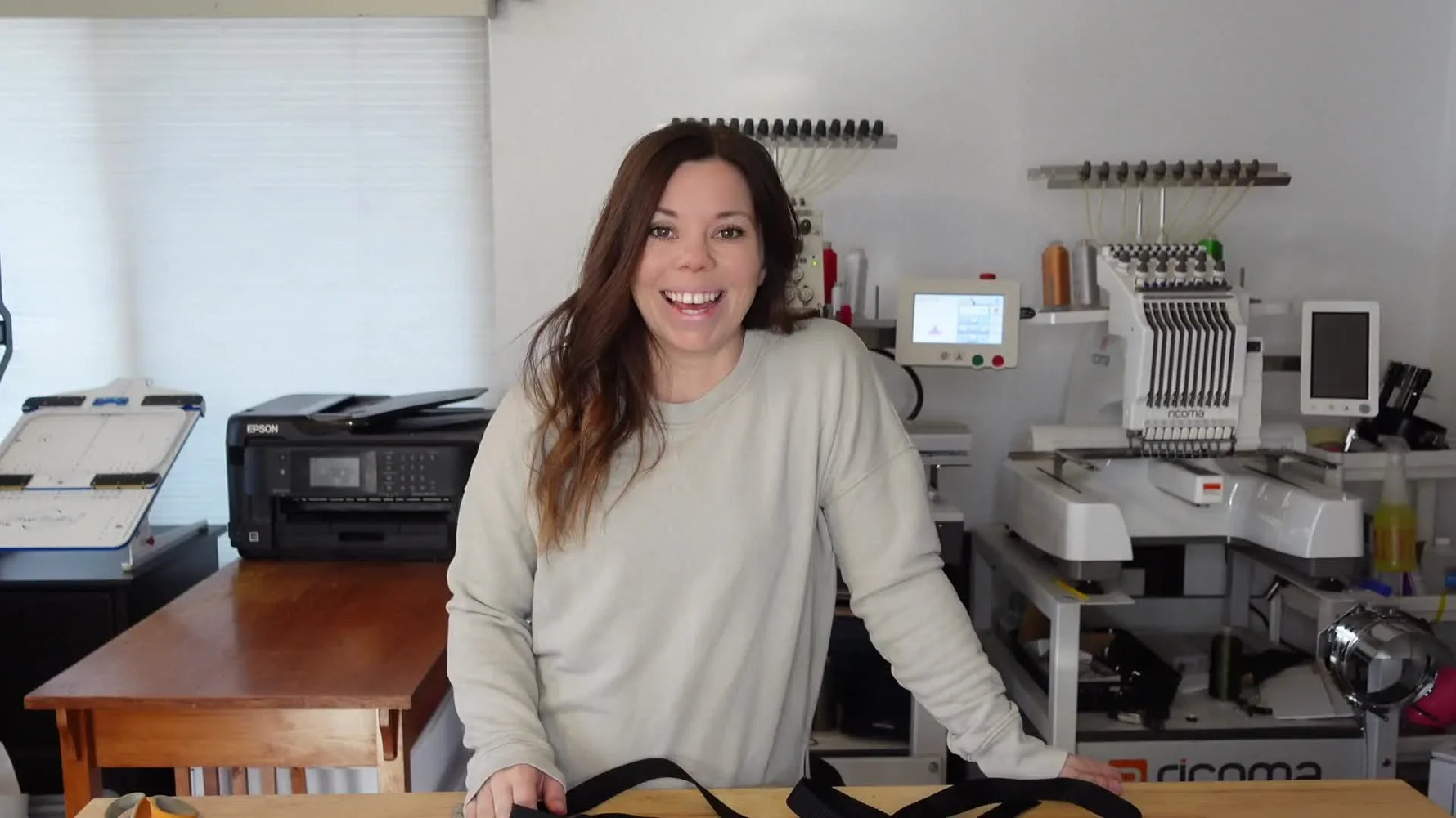 Woman in beige sweatshirt standing in an embroidery studio.