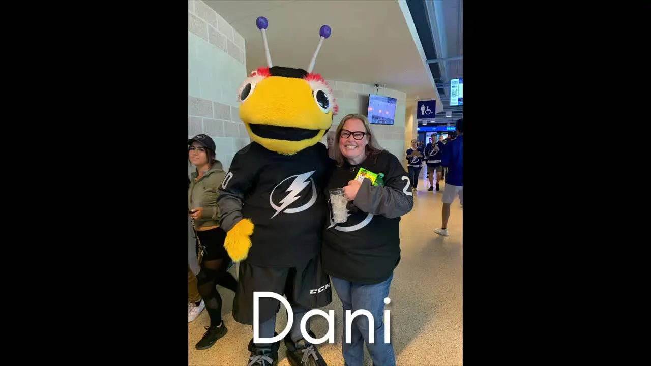 Woman in a black t-shirt standing next to a person in a bee mascot costume, smiling.
