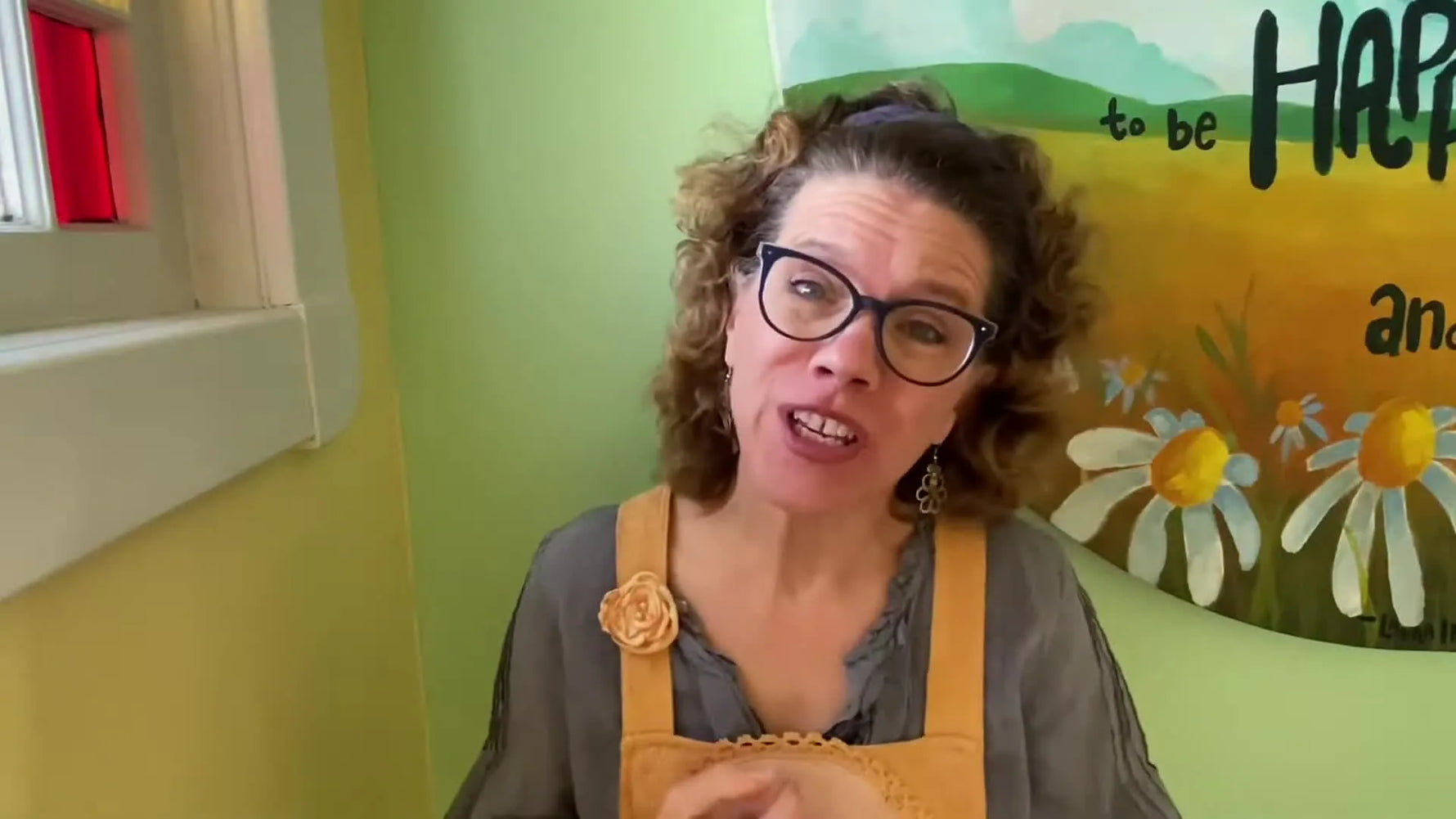 Angela Jean smiling at the camera, wearing glasses and a grey tunic over a white shirt.