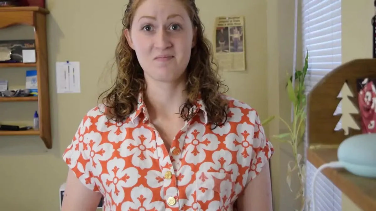 Woman in floral shirt smiling at camera in a home setting.
