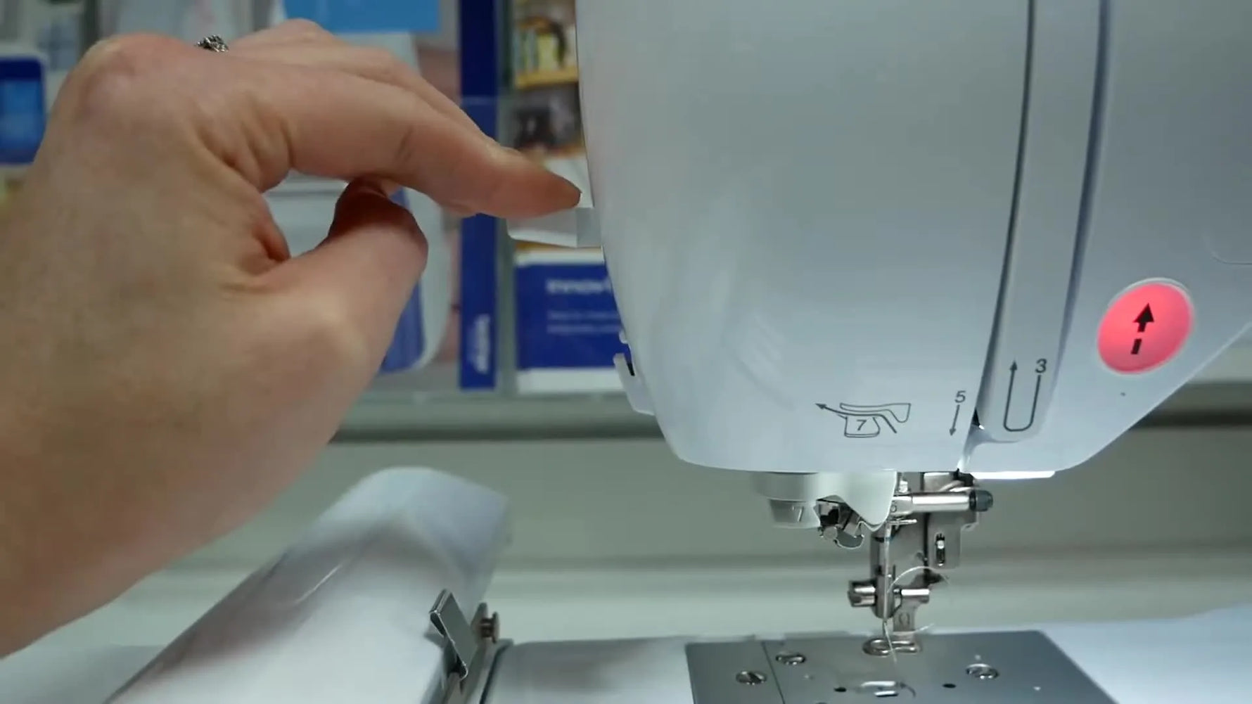 A close-up of the Brother Innov-is F440E actively stitching the first letter on hooped calico, showing the embroidery foot, moving needle, and stable fabric surface.