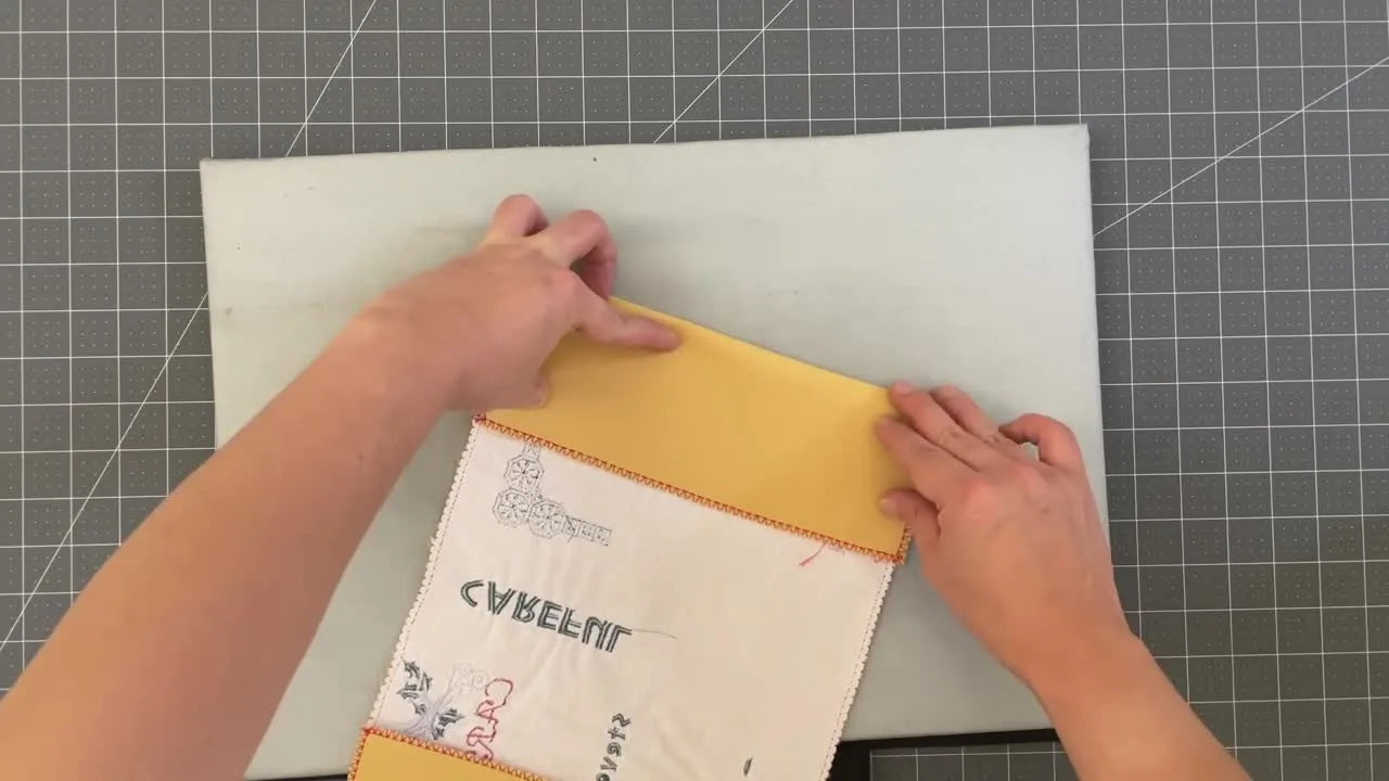 A finished yellow embroidered book cover with the word “CAREFUL” and floral motifs wrapped neatly around a hardcover book.