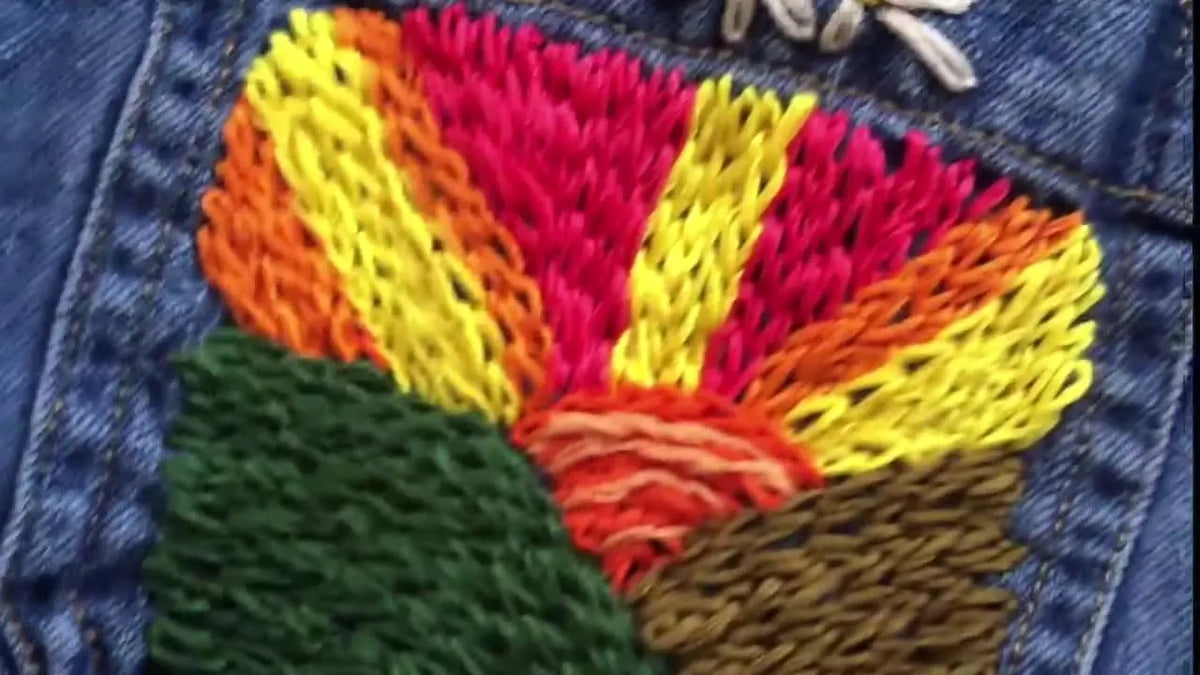 A close-up of a finished colorful embroidery of a sunrise on the pocket of a denim shirt.