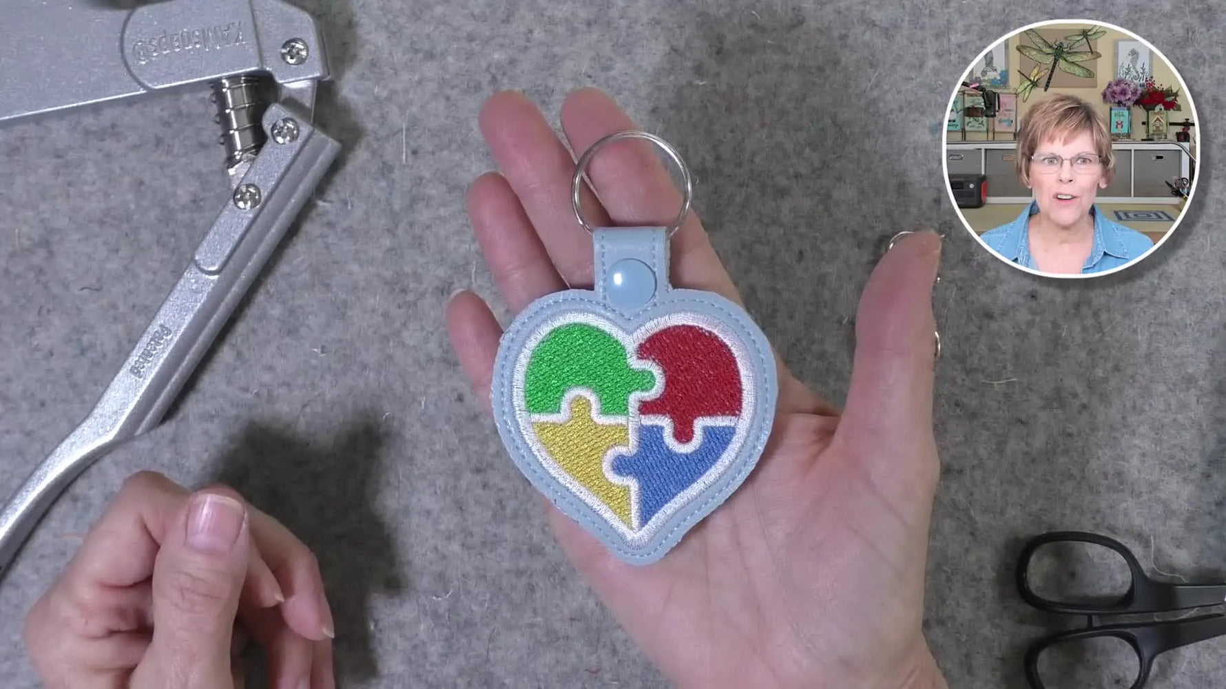 A finished Autism heart puzzle-piece key fob is held close to the camera, showing clean satin borders and completed hardware.